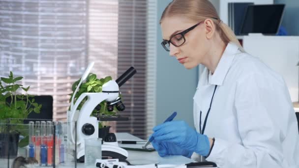 Profesora de química femenina usando pinzas para poner material orgánico en la diapositiva y mirar bajo el microscopio — Vídeos de Stock