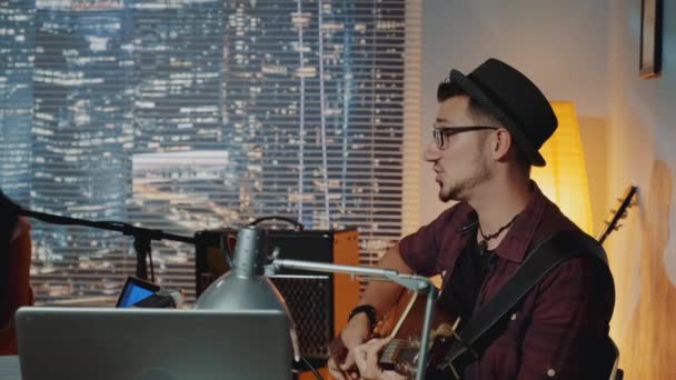 Profilnézet jóképű hipster énekel mikrofonba, és gitározik otthon stúdió — Stock videók