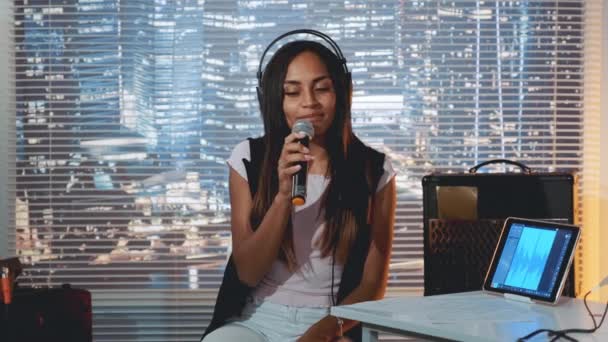 Kulaklıklı güzel siyah kız mikrofona şarkı söylüyor ve stüdyoda şarkı kaydediyor. — Stok video
