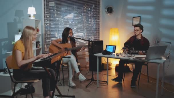 Allegro gruppo multirazziale di amici che cantano e suonano strumenti musicali in un accogliente studio domestico la sera — Video Stock