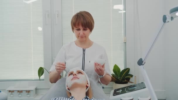 Косметик надевает маску со сливками на лицо женщины в салоне красоты — стоковое видео