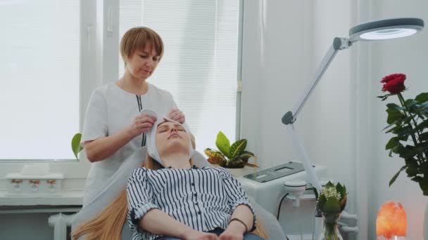 Косметик готовит женщину к очищению лица в салоне красоты — стоковое видео