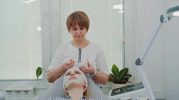 Schoonheidsspecialiste zet crème masker op vrouwen gezicht bij schoonheidssalon — Stockfoto