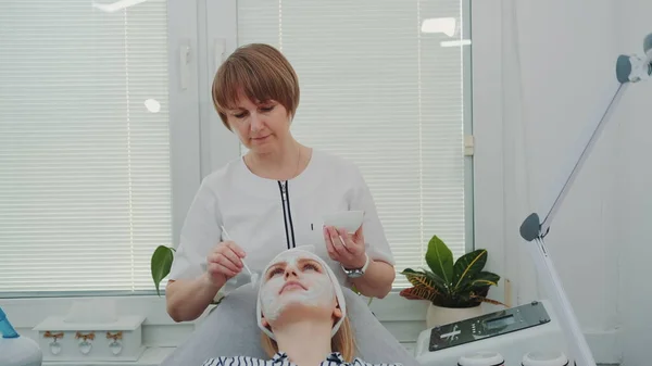 Schoonheidsspecialiste zet crème masker op vrouwen gezicht bij schoonheidssalon — Stockfoto