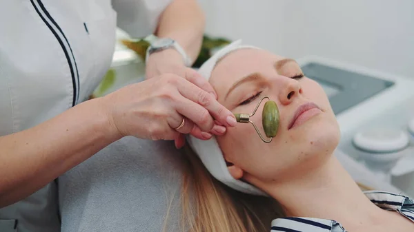 Close-up shot van gezichtsmassage met een jade roller op vrouwen gezicht op schoonheidssalon — Stockfoto