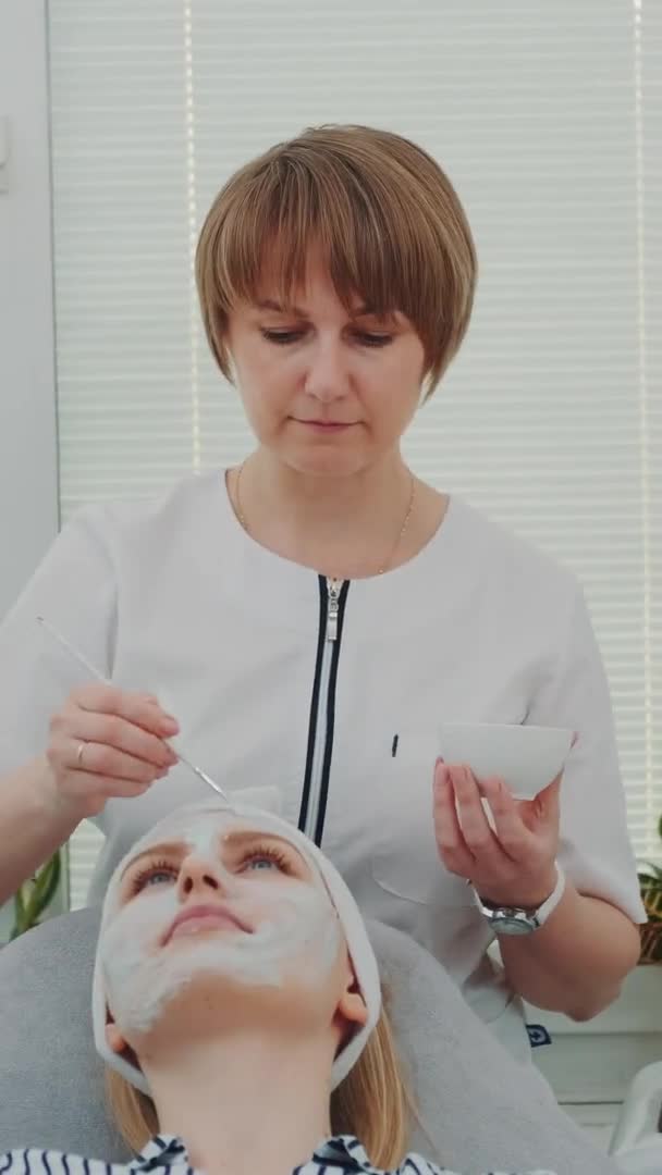 Schoonheidsspecialiste zet crème masker op vrouwen gezicht bij schoonheidssalon — Stockvideo