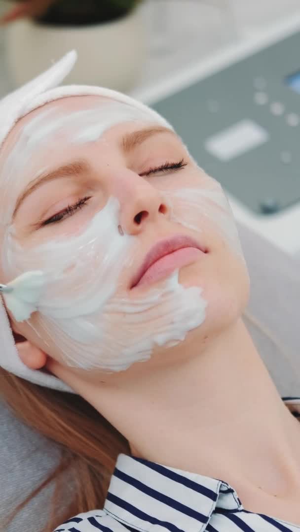 Mittlere Aufnahme einer Kosmetikerin, die im Schönheitssalon eine Creme-Maske auf das Gesicht von Frauen aufträgt — Stockvideo