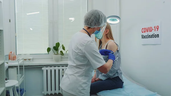 Tıbbi koruyucu giysiler içinde kadın doktor. Kadınlara iğne yapıyor. Koronavirüse karşı aşı yapıyor.