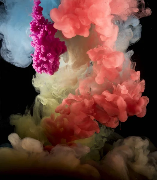 Colorful rainbow paint drops from above mixing in water. Ink swirling underwater.