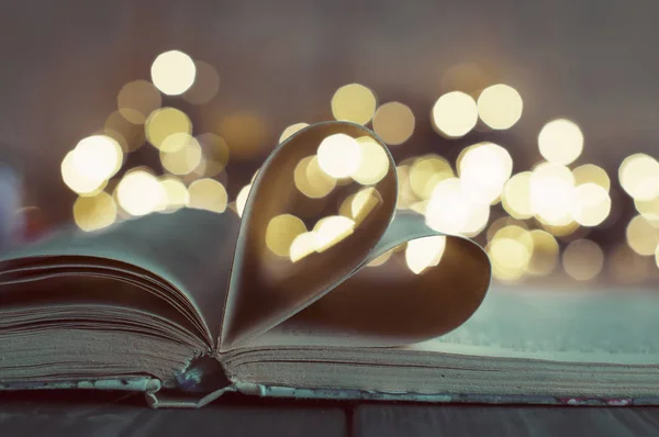 an open book with pages curved in shape of heart and bokeh light as background