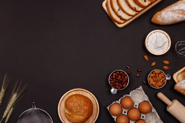 Homemade breads or bun, croissant and bakery ingredients, flour, almond nuts, hazelnuts, eggs on dark background, Bakery background frame, Cooking breakfast concept. Flat lay, Top view and copy space