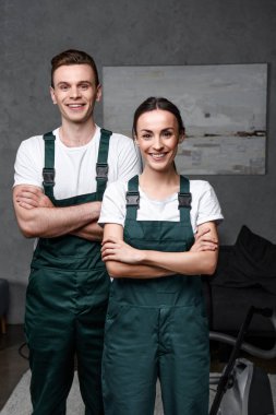 cheerful young professional cleaners standing with crossed arms and smiling at camera  clipart