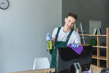 mutlu genç profesyonel süpürge bez deterjan ve temizlik bilgisayar monitörü ile ofiste holding