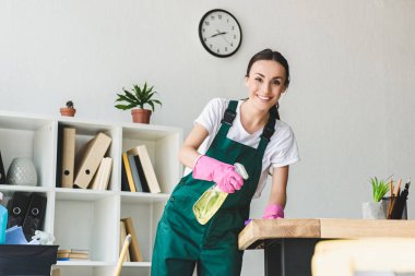 sprey şişe deterjan ile tutarak ve office temizlerken kameraya gülümseyen güzel genç süpürge