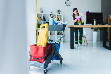 Genç kadın hademe çeşitli Temizleme Ekipmanı ile ofis temizliği