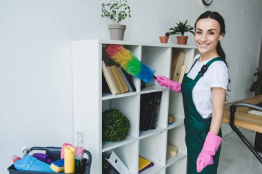 toz bezi tutarak ve Office rafları temizlerken kameraya gülümseyen güzel genç süpürge 