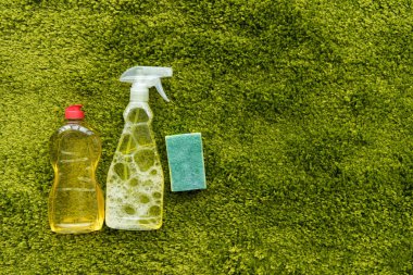top view of bottles with detergent and rag on green carpet with copy space 
