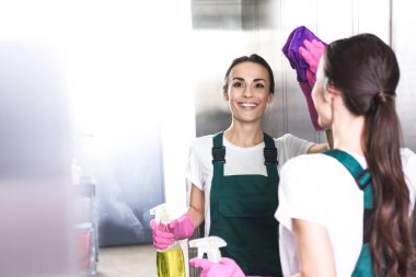 smiling young female cleaner washing elevator with rag and detergent clipart