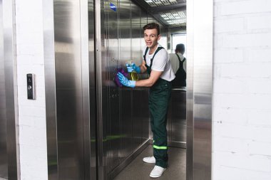 handsome young man cleaning elevator and smiling at camera    clipart