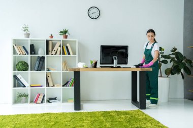 Lastik eldiven ve modern ofis masasında temizlik üniforma genç temizlik şirketi işçisi