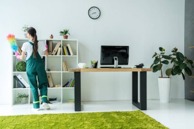 arkadan görünüşü genç süpürge toz bezi tutarak ve modern ofis temizliği