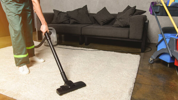 partial view of person using vacuum cleaner while cleaning white carpet 