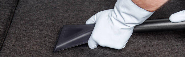 cropped shot of person in rubber gloves cleaning sofa with vacuum cleaner 