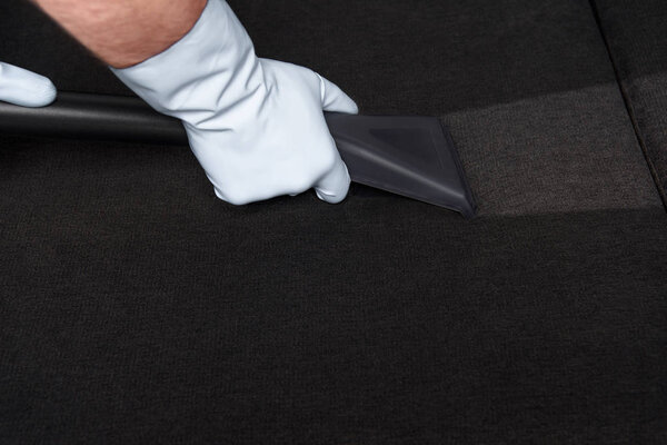 close-up partial view of person in rubber gloves cleaning sofa with vacuum cleaner 