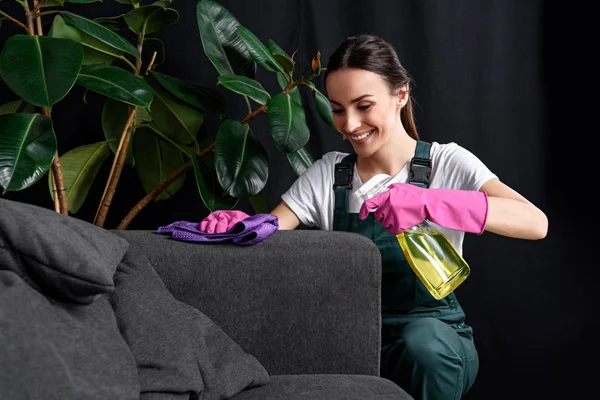 gülümseyen genç kadın kanepe bez ve deterjan sprey ile temizlik lastik eldiven