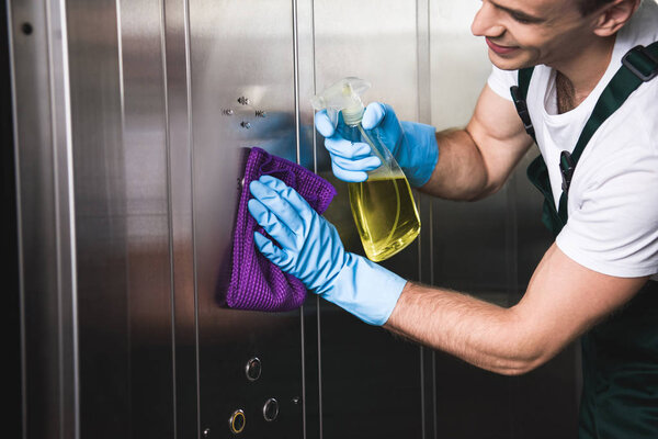 cropped shot of smiling young worker cleaning elevator with rag and detergent