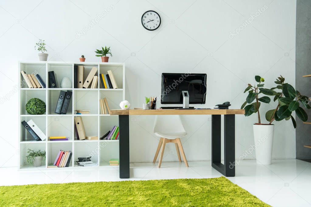 modern office interior with computer monitor on table and books with folders on shelves