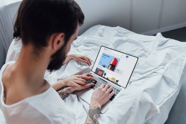 arkadan görünüşü yatakta yatarken, el ele tutuşarak ve ebay Web sitesinde ekran ile dizüstü bilgisayar kullanarak bir çift 