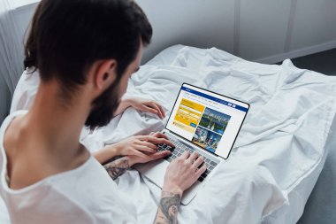 arkadan görünüşü yatakta yatarken, el ele tutuşarak ve rezervasyon Web sitesinde ekran ile dizüstü bilgisayar kullanarak bir çift 