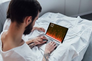 arkadan görünüşü yatakta yatarken, el ele tutuşarak ve ekranda online ticaret Web sitesi ile dizüstü bilgisayar kullanarak bir çift 
