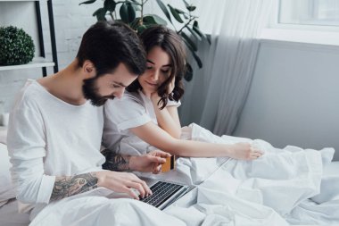 kredi kartı ve yatakta yatan ve online alışveriş yaparken laptop ile güzel genç Çift