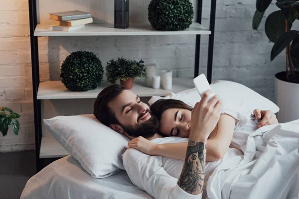 Yakışıklı Adam Yatakta Uyuyan Kadın Ise Smartphone Kullanarak — Stok fotoğraf