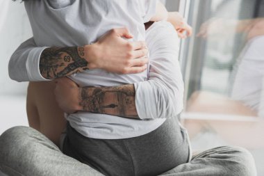 cropped view of tattooed man passionately hugging woman at home