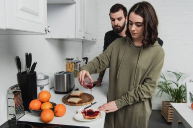 güzel kadın reçel tost üzerinde arka plan üzerinde adamla mutfakta kahvaltı sırasında dökülen