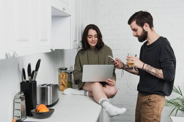 suyu içme ve mutfakta kahvaltı sırasında dizüstü bilgisayar kullanan kadın ise smartphone kullanarak adam