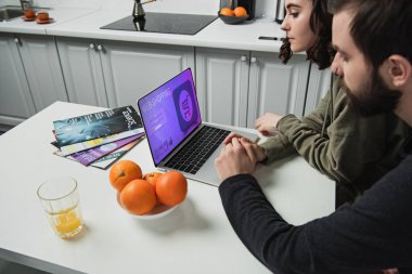 masada oturan ve mutfakta ekranda online alışveriş Web sitesi ile dizüstü bilgisayar kullanarak bir çift