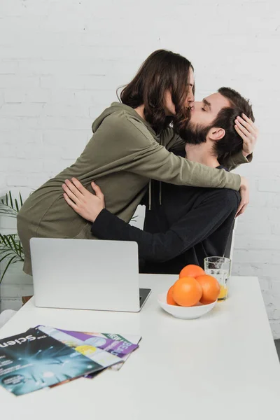 Beautiful Young Couple Hugging Kissing Table Laptop Oranges Breakfast Kitchen — Stock Photo, Image