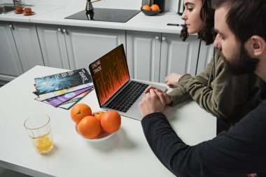 masada oturan ve mutfakta ekranda online ticaret Web sitesi ile dizüstü bilgisayar kullanarak bir çift
