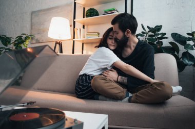 güzel genç çift kanepede oturan, sarılma ve vinil için bekleyen oturma odasında kaydetmek
