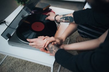 cropped view of tattooed couple putting vinyl record on record player  clipart