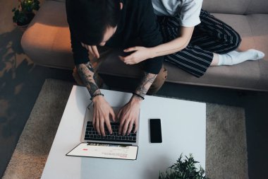 Çift oturma ang airbnb Web sitesinde evde ekran ile dizüstü bilgisayar kullanırken sarılma görünümünü kırpılmış 