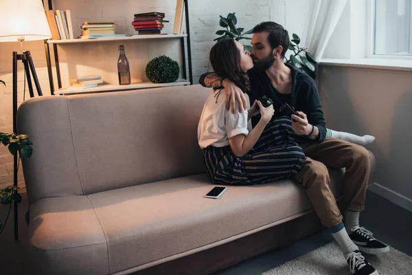 美しい若いカップルのキスとハグ ジョイスティック タイプのリビング ルームでソファの上に座っている間 — ストック写真