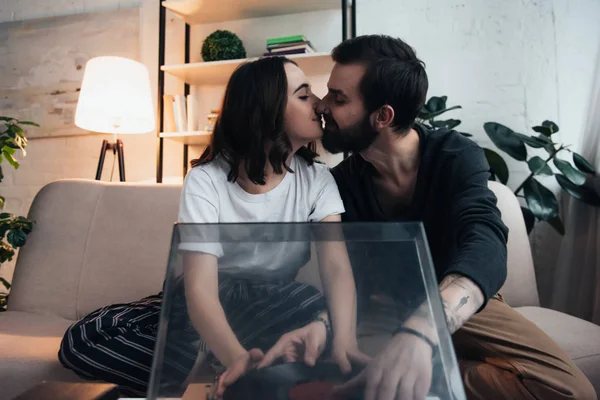 beautiful couple kissing and putting vinyl record on record player in living room