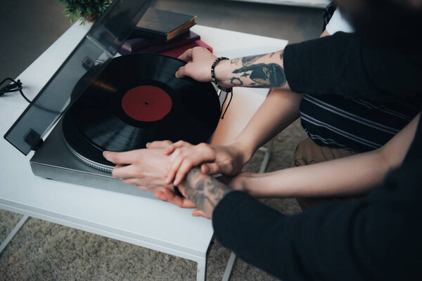 cropped view of tattooed couple putting vinyl record on record player 