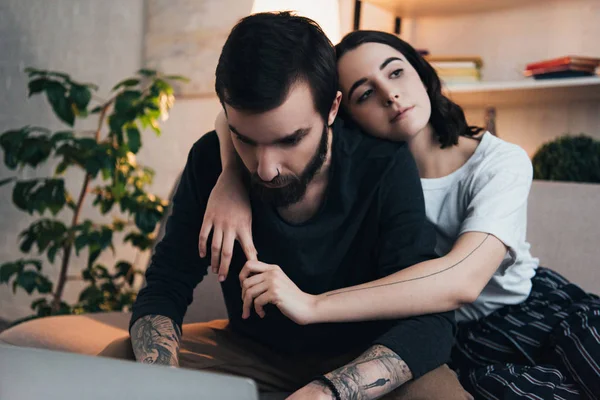 Belo Jovem Tatuado Casal Abraçando Enquanto Sentado Sofá Sala Estar — Fotografia de Stock