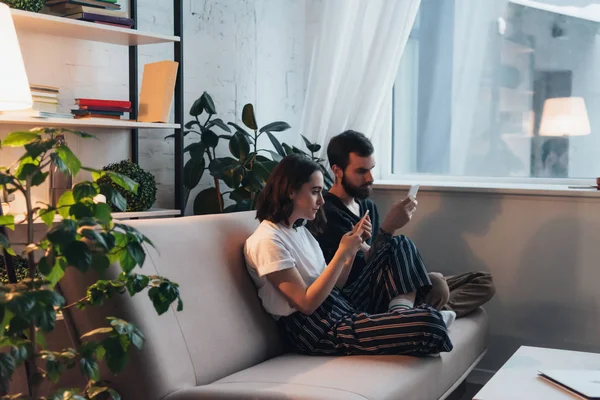 Pareja Joven Sentada Sofá Usando Teléfonos Inteligentes Sala Estar —  Fotos de Stock